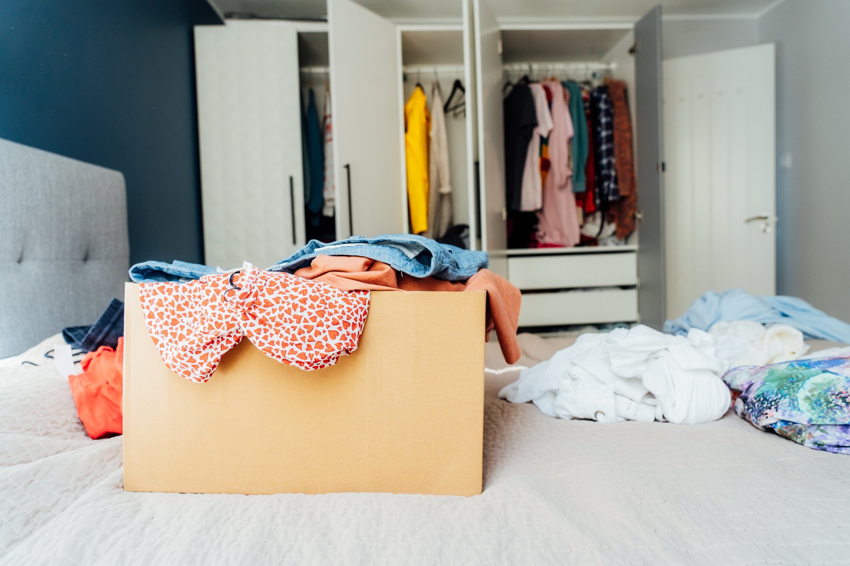 A Cardboard Box of Selected Clothes for Donating to a Charity Shop Standing on the Bed. Decluttering, Sorting Clothes, and Cleaning up. Reuse, Second-Hand. Conscious Consumer, Sustainability.